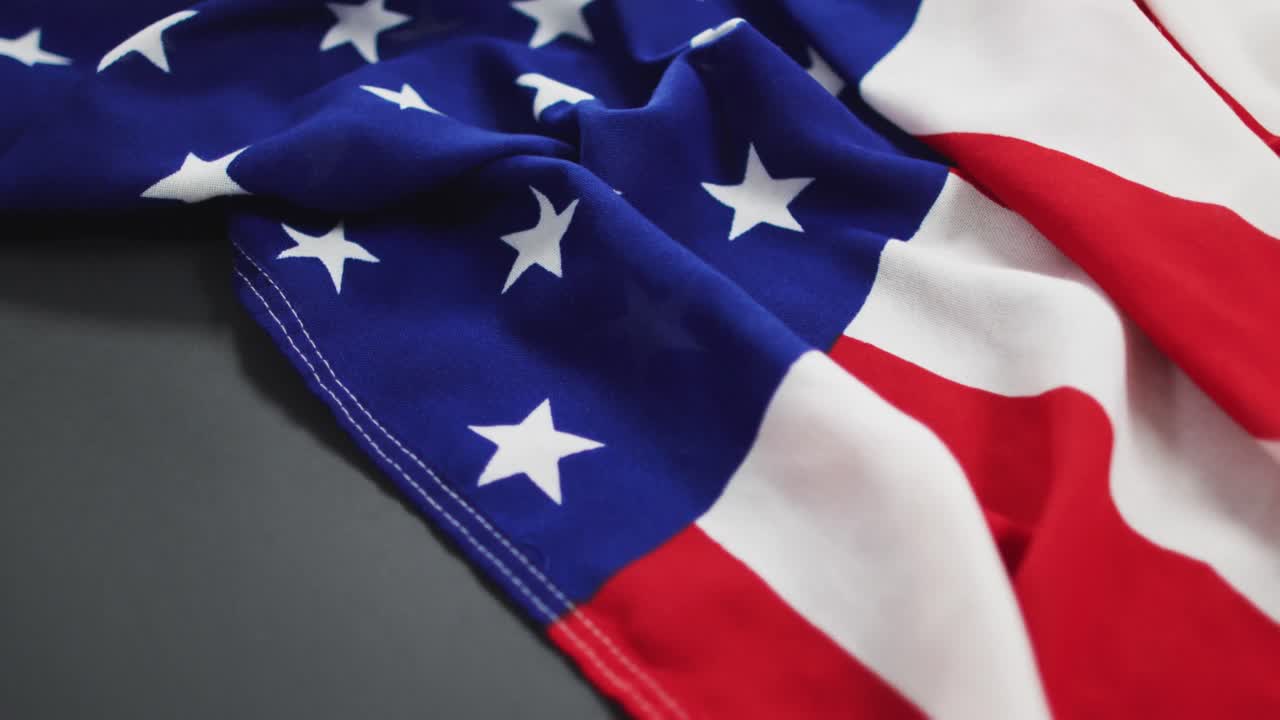 Bandiera americana spiegazzata con stelle e strisce adagiata su sfondo grigio.
