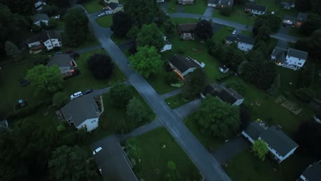 aerial flyover housing area in idyllic green suburbia. top down. dusk scene in summer. one family houses and yards in quiet area of usa