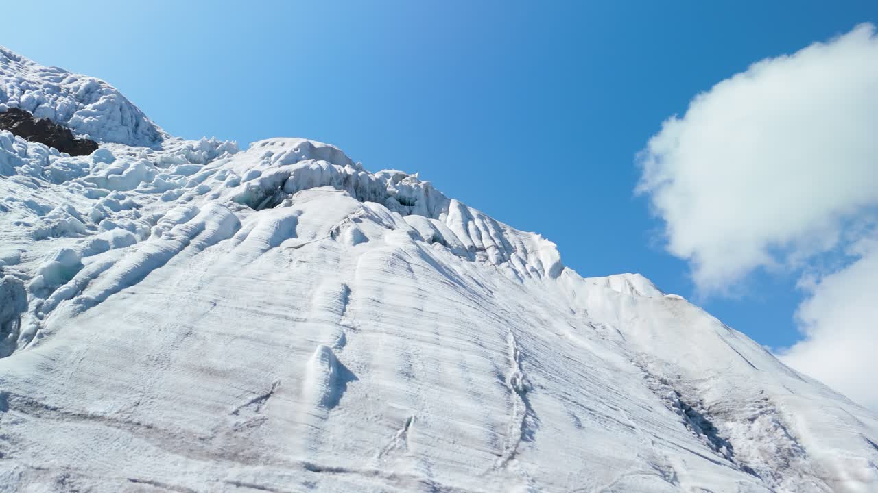 Aerial shot rising with a low angle against the sky, revealing the icy slopes and crevasses of Montaña Mateo glacier in Peru's Cordillera Blanca