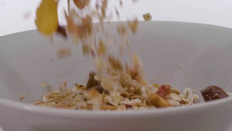 Close-up-of-white-rotating-bowl-against-white-background-while-vegan-or-vegetarian-cereal-with-fruit-falls