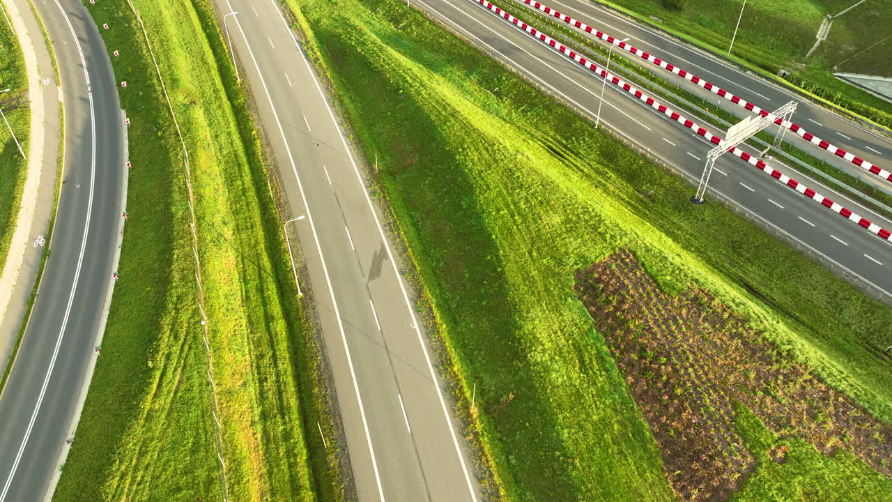 Aerial top-down view of a modern highway (S6 road) cutting through steep green embankments and farmland. Features a single car and traffic barriers