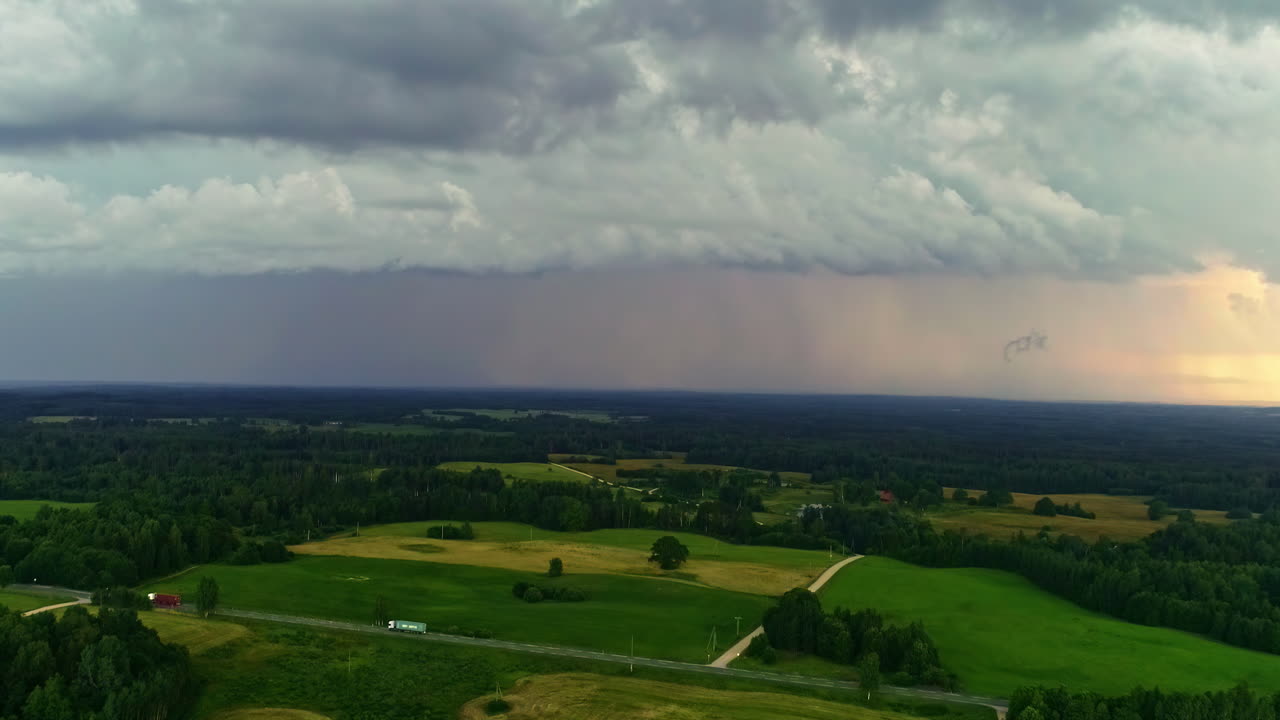 Bedrohliche Sturmwolken, ferner Regen über grünen Feldern und Wäldern, Drohnenansicht
