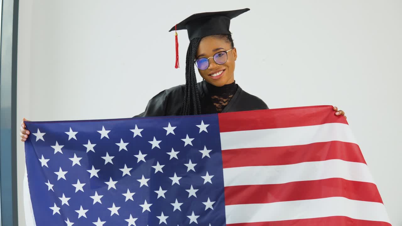 feliz elegante estudiante afroamericana en uniforme de graduado sosteniendo nuestra bandera delante de ella. el plan promedio