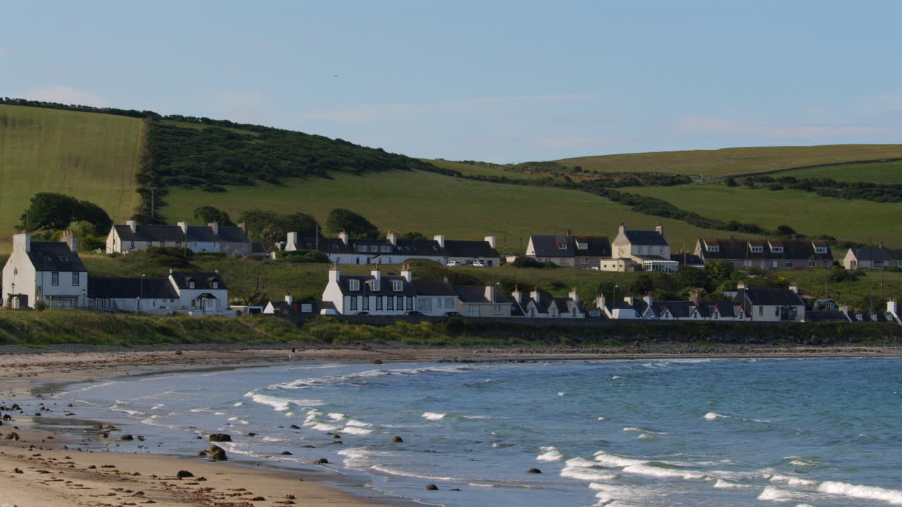 Campo lungo di case a Port Logan con la spiaggia in primo piano.