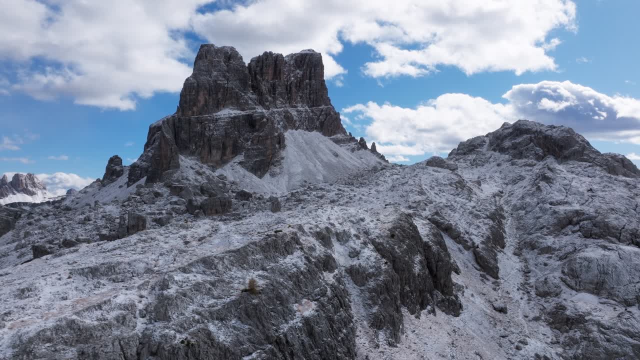 A drone flight near Cortina d'Ampezzo in late October, the peak is covered with snow on a partly cloudy day