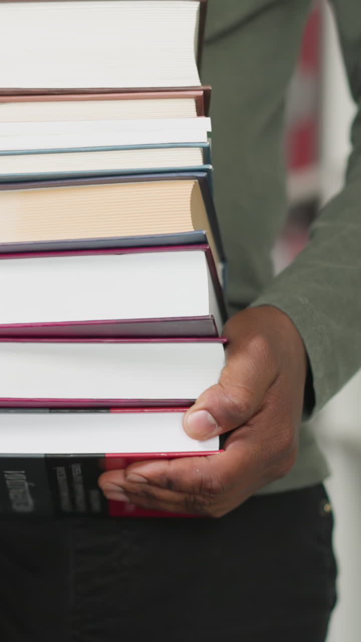 hombre negro lleva una pila de libros en una tienda de primer plano. maestra afroamericana sostiene una gran pila de libros de texto caminando entre estanterías. trabajo de bibliotecario