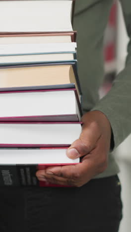 black man carries book stack in store closeup. african american teacher holds large textbook pile walking between shelving. librarian work