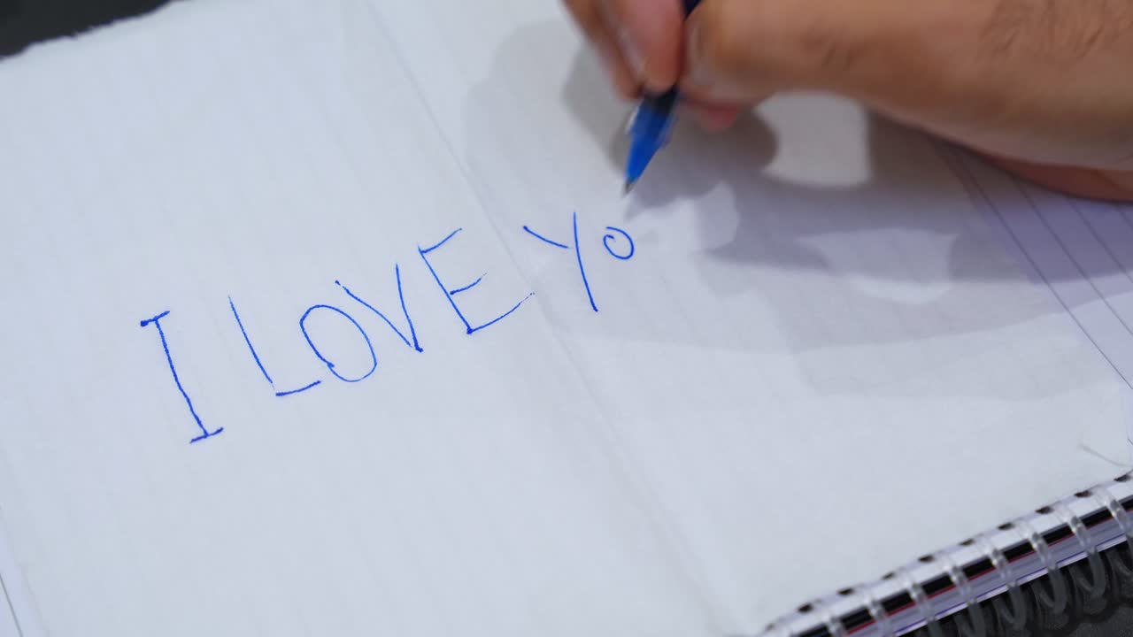 Close-up of hand writing “I Love You” in blue ink on napkin paper. Perfect for romantic, heartfelt, cinematic, or Valentine’s Day content.