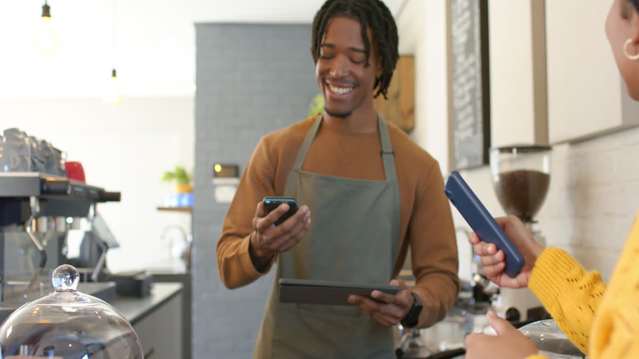 Female customer tapping phone and paying for takeaway cups as barista holding scanner at counter