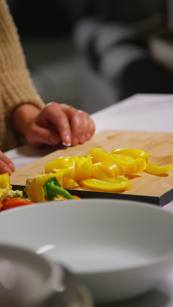 Vertikální video: Detail ženy doma v kuchyni, jak připravuje zdravou čerstvou zeleninu pro vegetariánské nebo veganské jídlo a vkládá nakrájené žluté papriky do misky