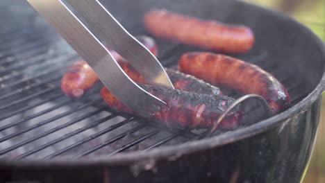 slow motion of tongs picking up a gristly sausage from smokey bbq grill