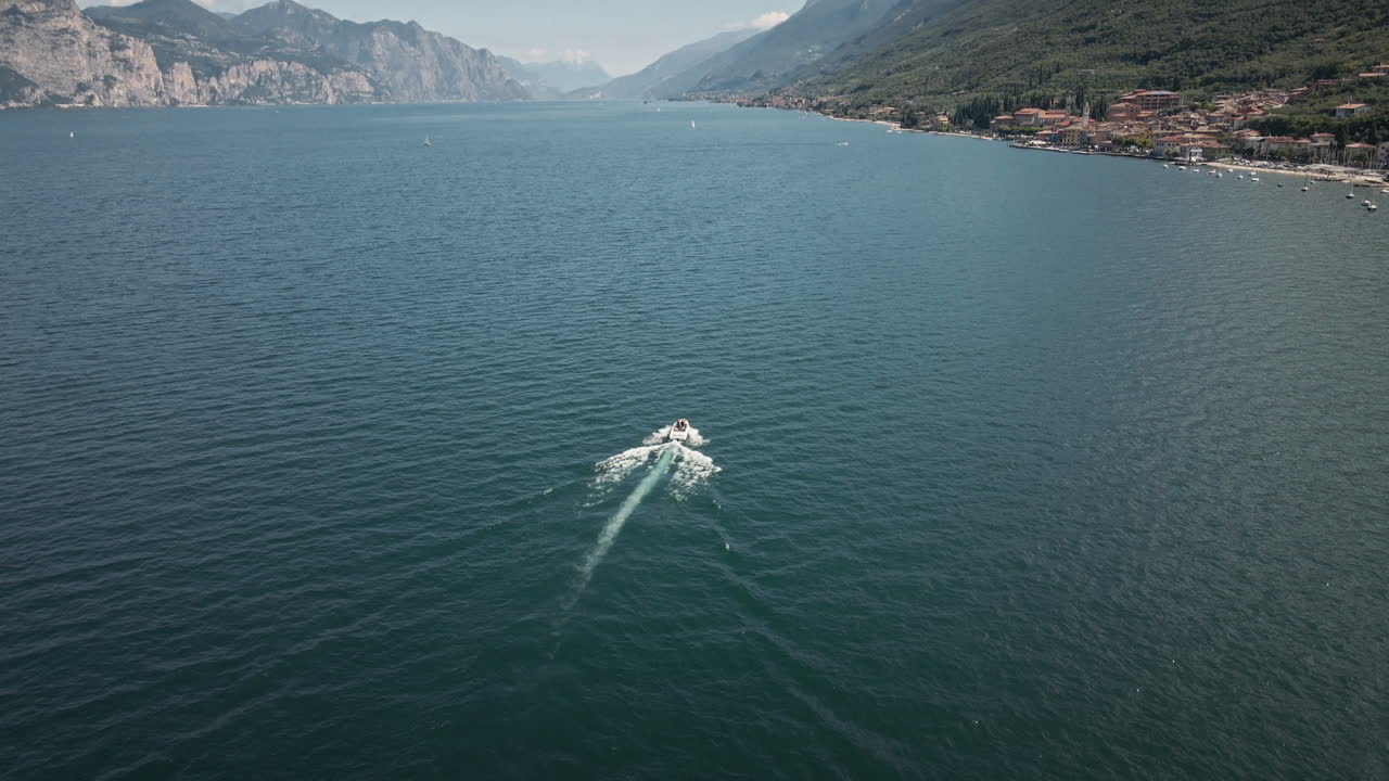 Un energico drone 4K UHD si alza mentre segue un motoscafo in velocità, rivelando lunghe scie bianche su acqua blu calma, ideale per promozioni di viaggio, introduzioni d'azione e branding marino.