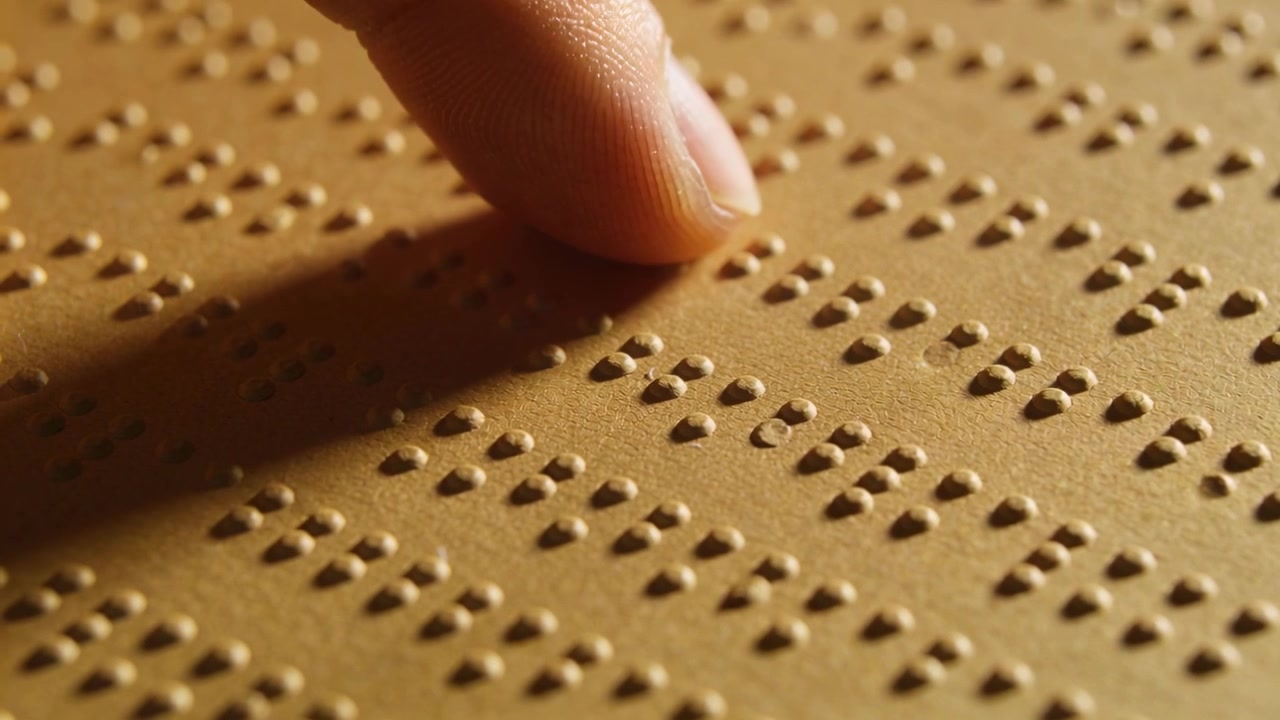 Un doigt glissant balaye une feuille à points en relief sur une surface de lecture après un repos, explorant un texte en braille.