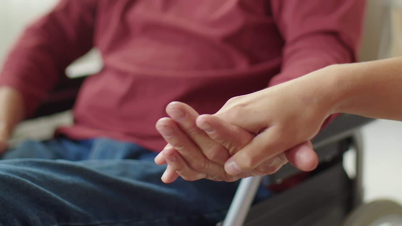 Caregiver Holding Hand of Elderly Man in Wheelchair