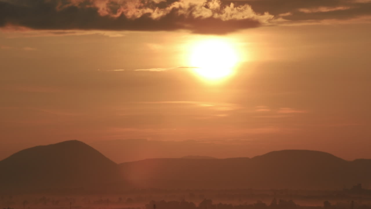Time lapse of golden sunrise rising above mountain silhouettes, capturing warm light, atmospheric clouds and serene landscape that symbolizes renewal, energy and natural beauty