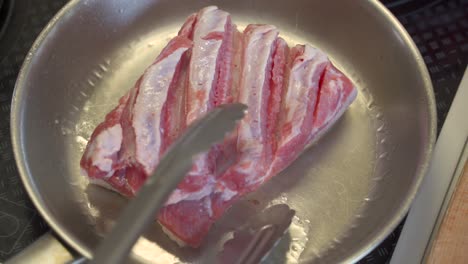 vista de arriba hacia abajo del corte de la panceta de cerdo que se voltea sobre una bandeja de acero inoxidable y se voltea para revelar el dorado