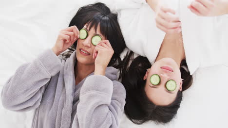 happy biracial mother and adult daughter taking cucumber slices from eyes and laughing, slow motion