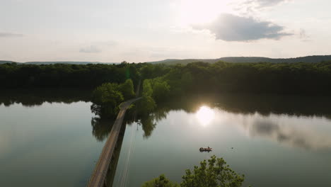 Utility-poles-and-footbridge-over-tranquil-lake-during-bright,-vibrant-sunset