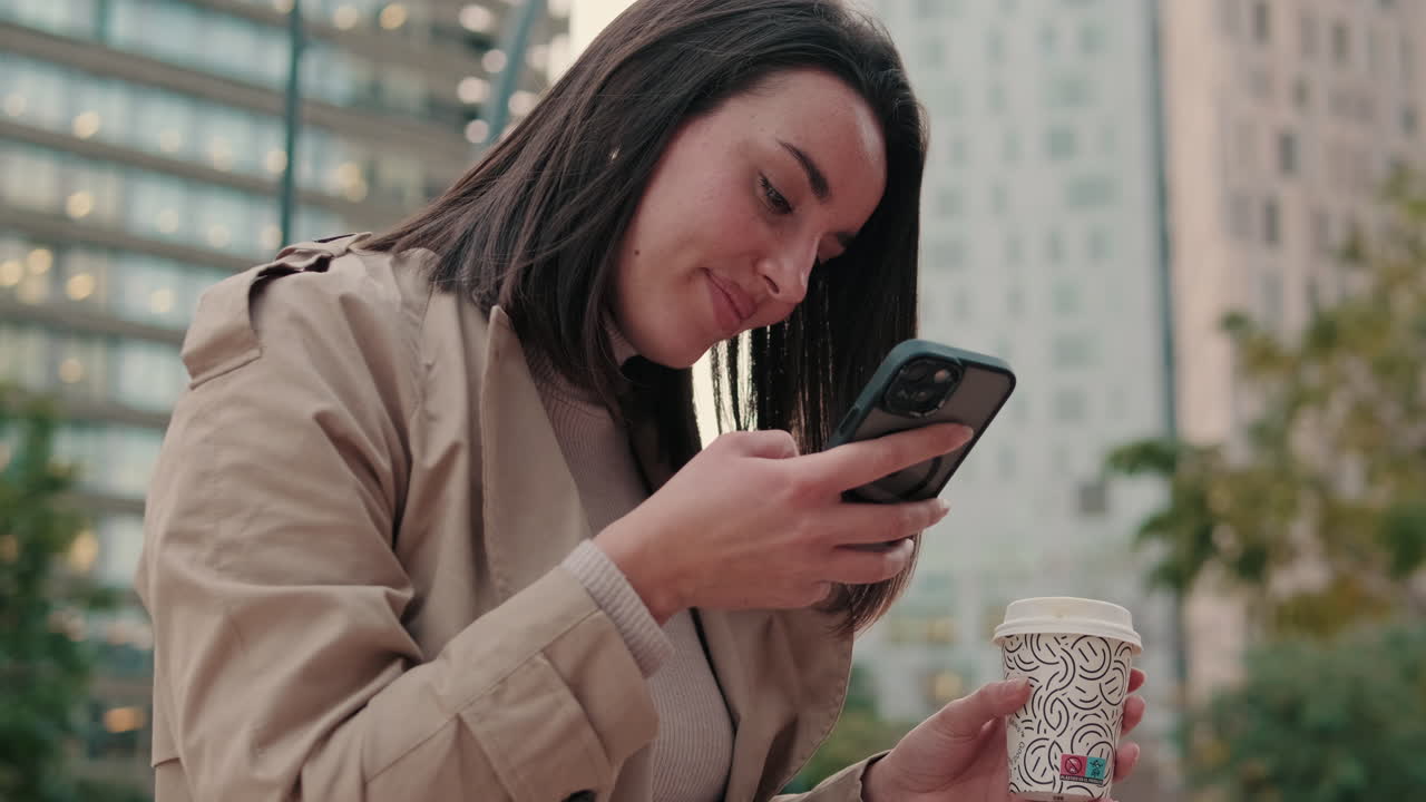 Giovane donna sorridente che manda messaggi al telefono con un caffè in città