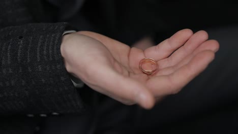 un hombre aprieta dos anillos de bodas en su mano. primer plano