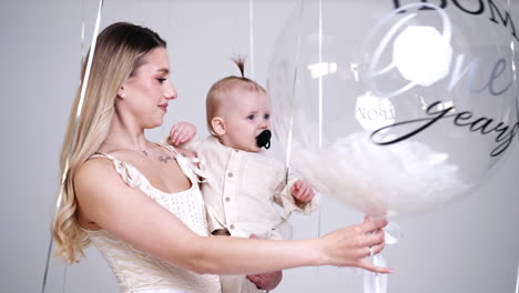 mother is holding her baby in hands. cheerful child grabs the big balloon. studio footage.