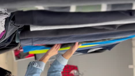 young woman buying used sustainable clothes from second hand charity shop. sale, shopping, fashion and people concept – woman chooses clothes in vintage clothing store. vertical video.