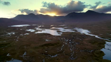 een drone rolt langzaam naar rechts links hoog boven een waterrijk landschap van eilanden en veenmoerassen omgeven door zoet water en kijkend naar bergen bij zonsondergang