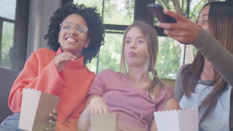 happy diverse teenager girls friends eating popcorn and watching tv at home, slow motion