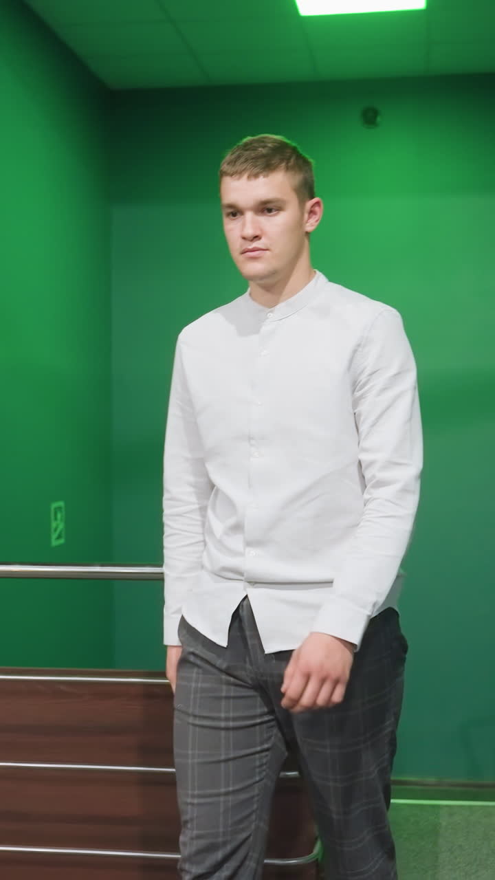 fotografía frontal de un tipo con camisa y pantalones subiendo las escaleras, moviéndose hacia la sala de billar. paso confiado con expresión seria. la iluminación verde arroja un brillo ambiental. la mano toca la mesa de billar verde