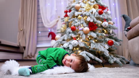 joyful baby boy sitting on the soft fluffy plaid. beautiful christmas tree at backdrop.