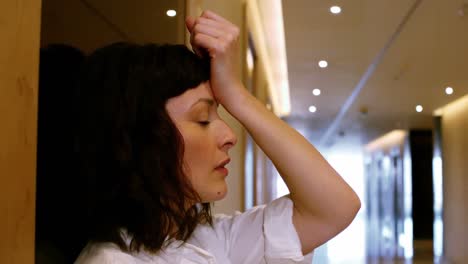 Unhappy-woman-leaning-against-the-wall-in-the-office-corridor