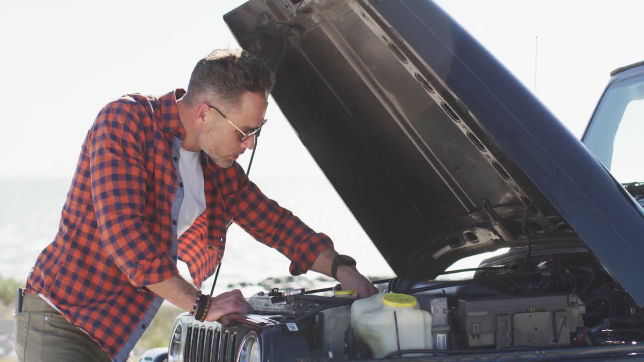 Caucasian man repairing broken down car with open bonnet on sunny day at the beach