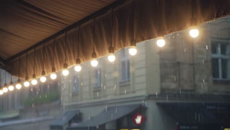 decorative lamps are hanging in the row and lighting on the background of the rain. raindrops are falling on the roof of the summer terrace of a cafe which is decorated with a row of lanterns