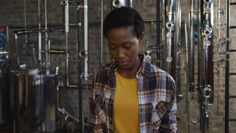 Portrait-of-african-american-woman-working-at-gin-distillery-holding-equipment-and-smiling-to-camera