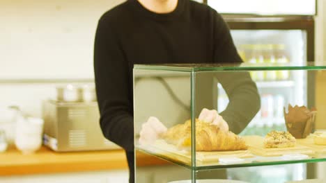 hombre manteniendo bandeja de croissants en el caso de exhibición de la cafetería