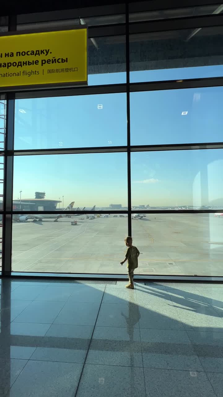 A young boy at an airport window looking at planes