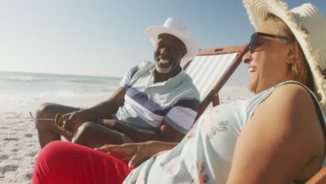 Lächelndes-älteres-Afroamerikanisches-Paar,-Das-Auf-Sonnenliegen-Am-Sonnigen-Strand-Liegt