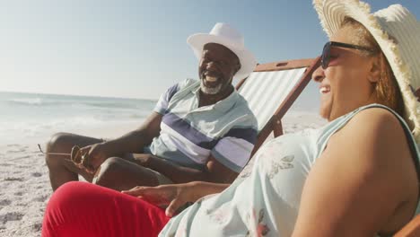 un couple senior afro-américain souriant allongé sur des chaises longues sur une plage ensoleillée
