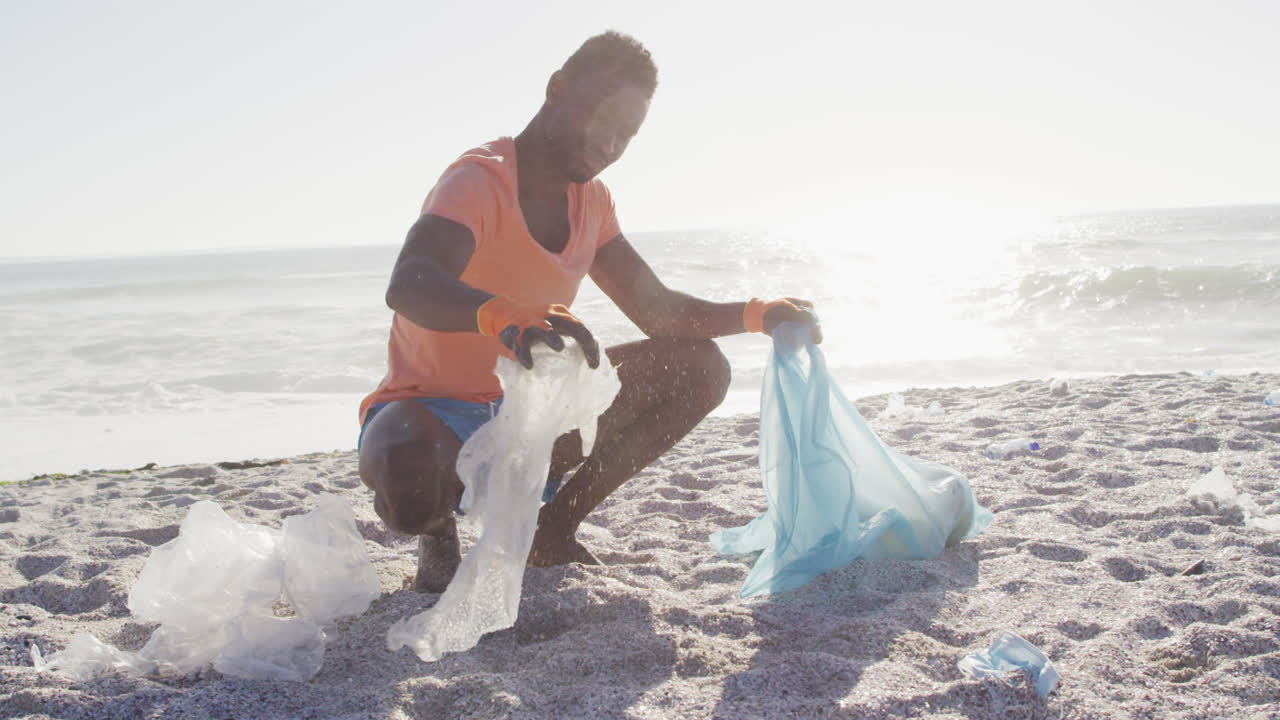 Uomo afroamericano che differenzia i rifiuti con i guanti su una spiaggia soleggiata