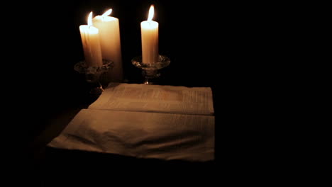 Holy-Bible-Lit-by-Candle-Light-in-a-Hidden,-Dark-Place-:-Pan-Slow-Right