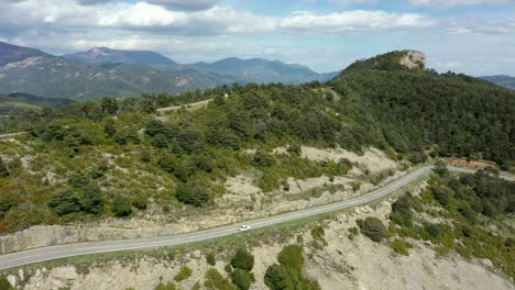 Old-white-car-broken-down-on-long-lush-mountain-valley-road-with-nobody-around-aerial-view