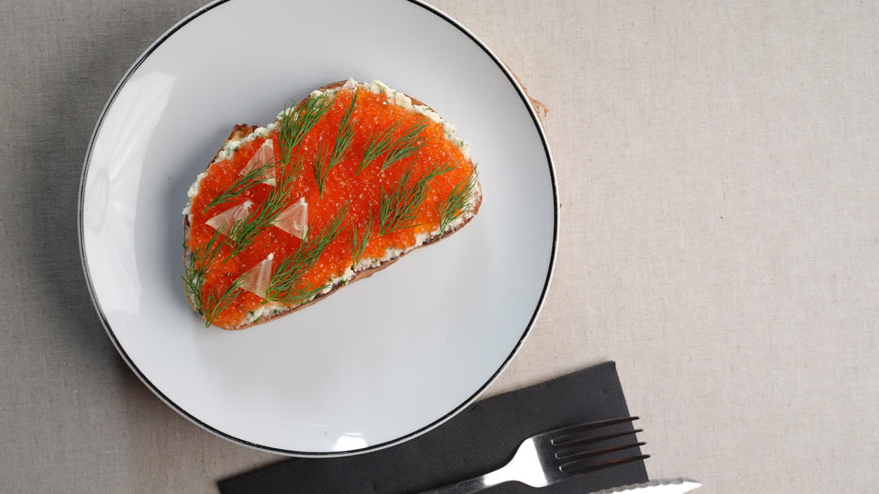 Creamy toast topped with rich red caviar, delicate lemon slices on white plate, complemented by sleek black cutlery, featuring classic Eastern European flavor profile