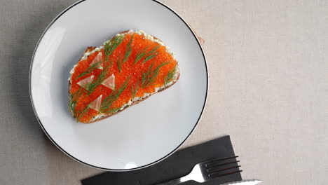 creamy toast topped with rich red caviar, delicate lemon slices on white plate, complemented by sleek black cutlery, featuring classic eastern european flavor profile