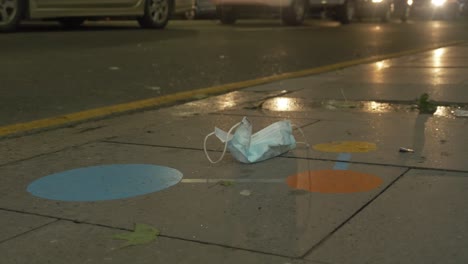 used disposable face mask lying on roadside blowing in the wind at night - coronavirus pandemic - inner city sydney, nsw, australia . - close up shot