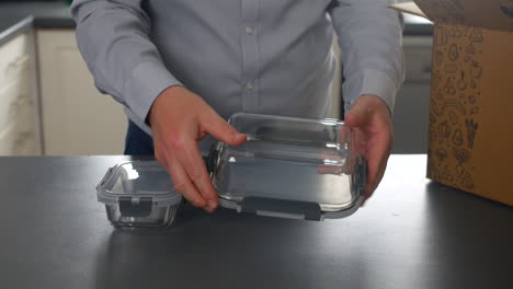 A-man-holding-a-glass-container-and-its-lid-in-a-modern-kitchen,-preparing-for-food-storage