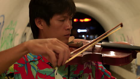 primer plano de un hombre cautivado mientras toca el violín en un túnel de graffiti
