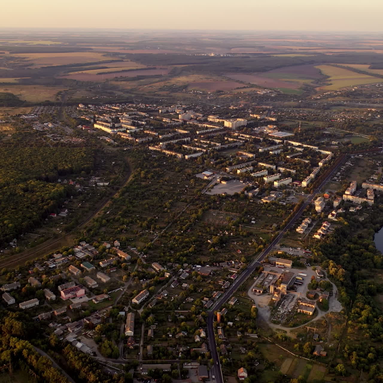 Aerial footage over small town in nature. Flight over the small buildings among fields in summer. Aerial view.