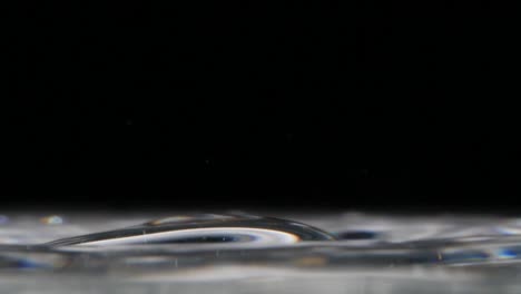 Close-up-on-water-drops-bouncing-on-a-glassy-water-surface,-copyspace