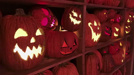 Espeluznantes-Cabezas-De-Calabaza-De-Halloween-En-El-Tablero-De-La-Estantería-En-El-Interior,-Iluminadas-Con-Velas-En-La-Oscuridad