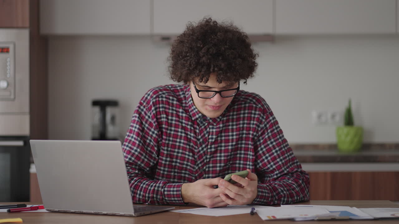 Young man with smartphone in his hands. Modern businessman or student at home office. Freelancer at work. Young student man study at home with laptop and uses a smartphone